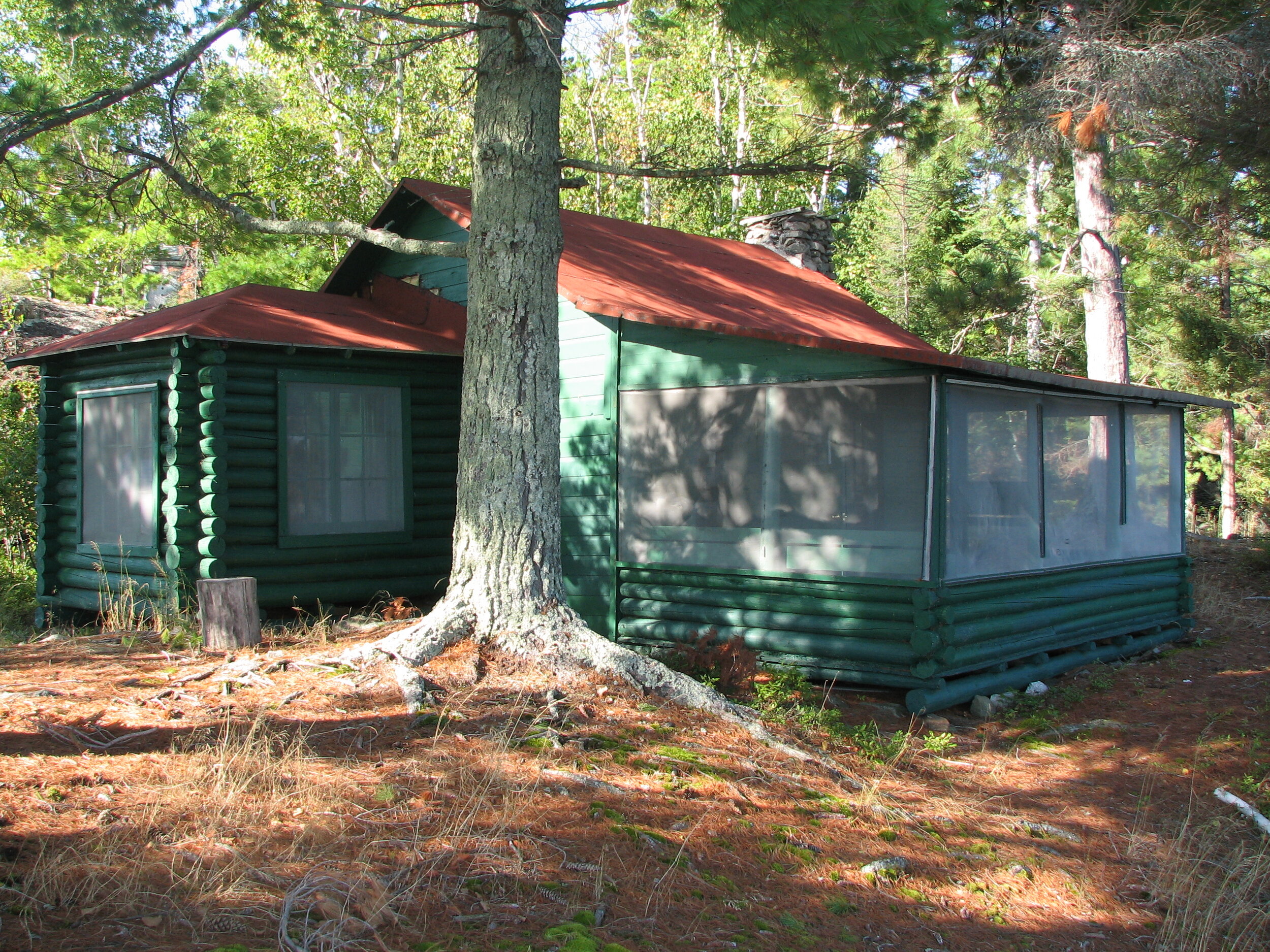 Photograph of Jun Fujita's Rainy Lake cabin. It has painted green log walls and a light red roof. 
