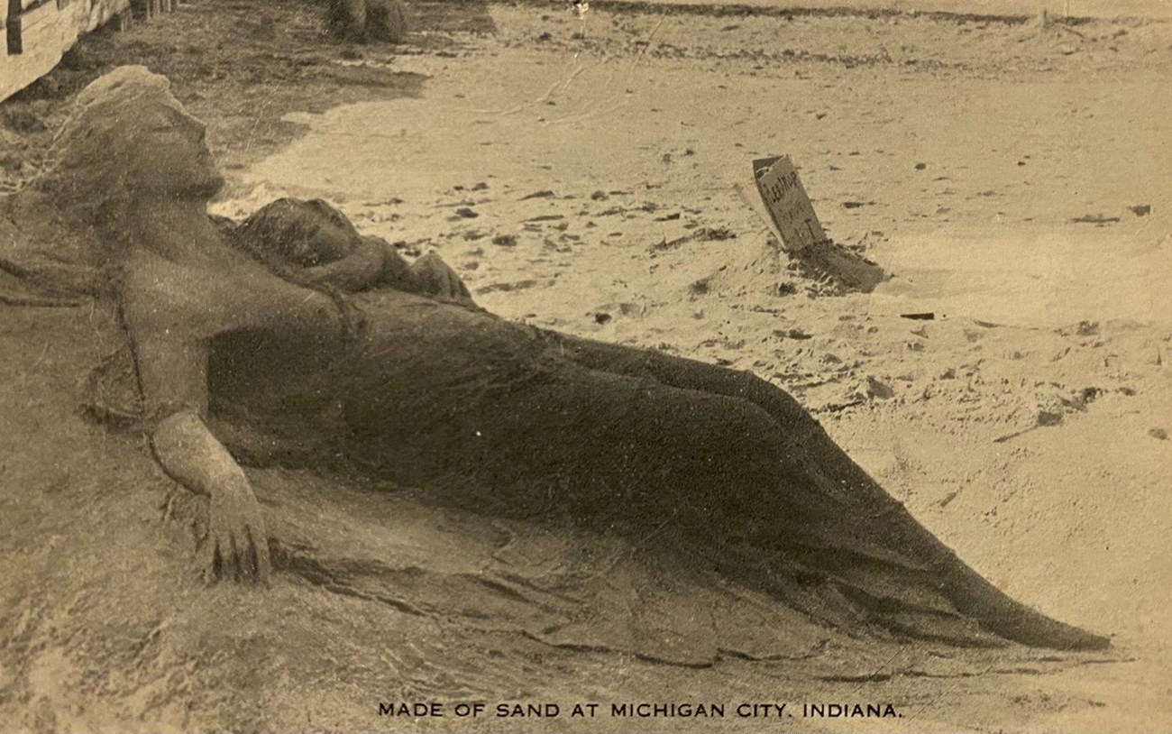 Old photo of a women on the beach with a baby made of sand.