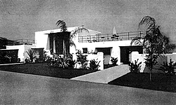 old black and white picture of flat roofed house with large windows with palm trees in landscaping