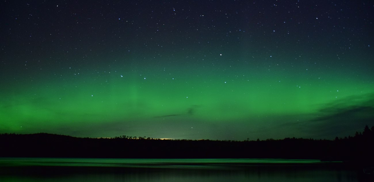 Green glowing northern lights across the night sky.