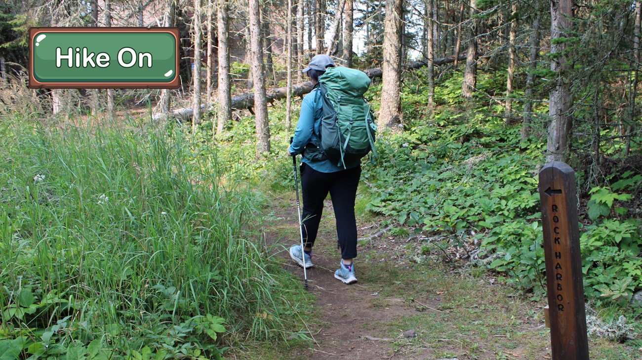 A person wearing a large backpack hikes on a trail next to a sign that says "Rock Harbor" with an arrow.