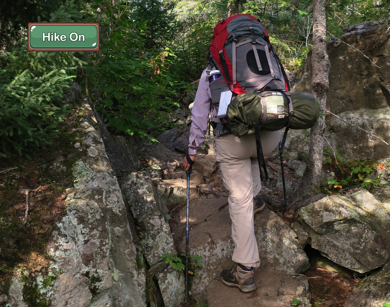 A person wearing a large backpack hikes over some large boulders.