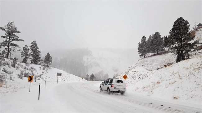 A white-colored park ranger truck drives along a mountainous highway during a snow storm.