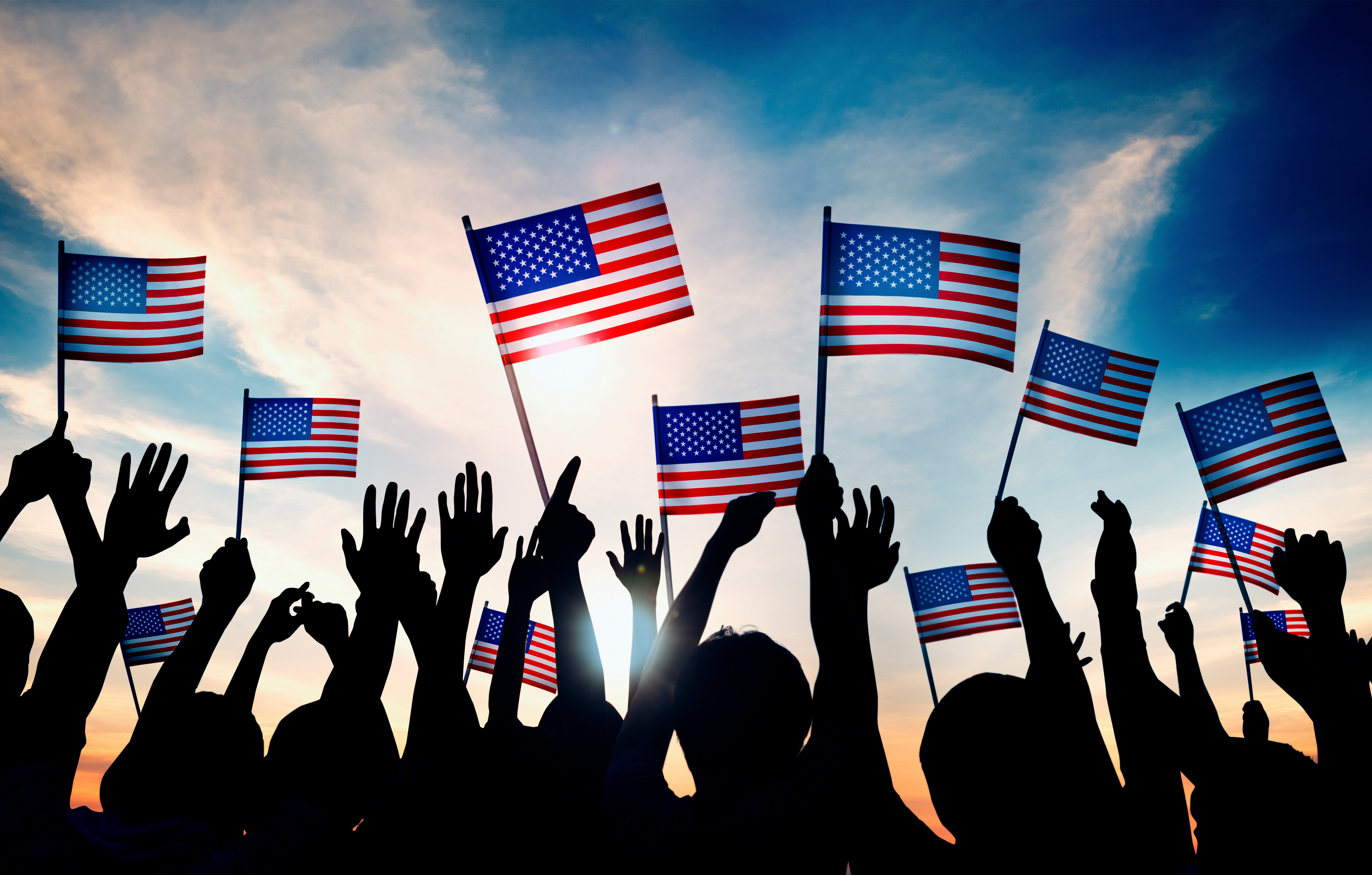 Arms waving small US flags, sky in the background