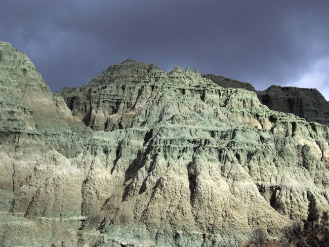 Blue, green, and tan rocks eroding into spire shapes with a dark gray-black sky above.