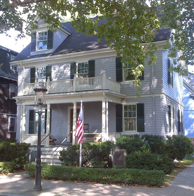 The front facade of JFK NHS a grey house with green shutters