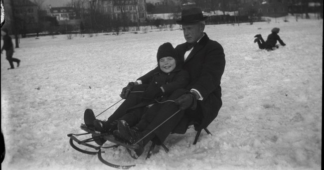 A black-and-white photo of Rosemary Kennedy sledding as a child with a family friend.