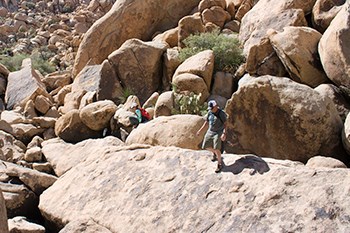 two people hiking on rocks, surrounded by many large boulders