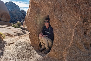 A visitor crouches in a cavity in a rock near a trail