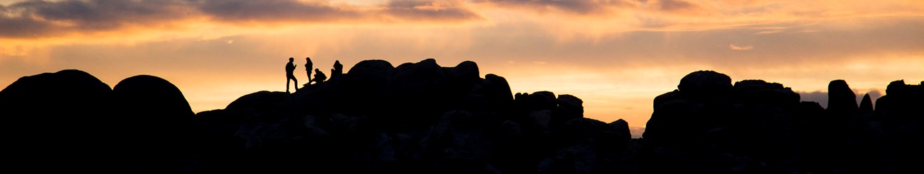 A silhouette of three people at the top of rocks as the sunsets