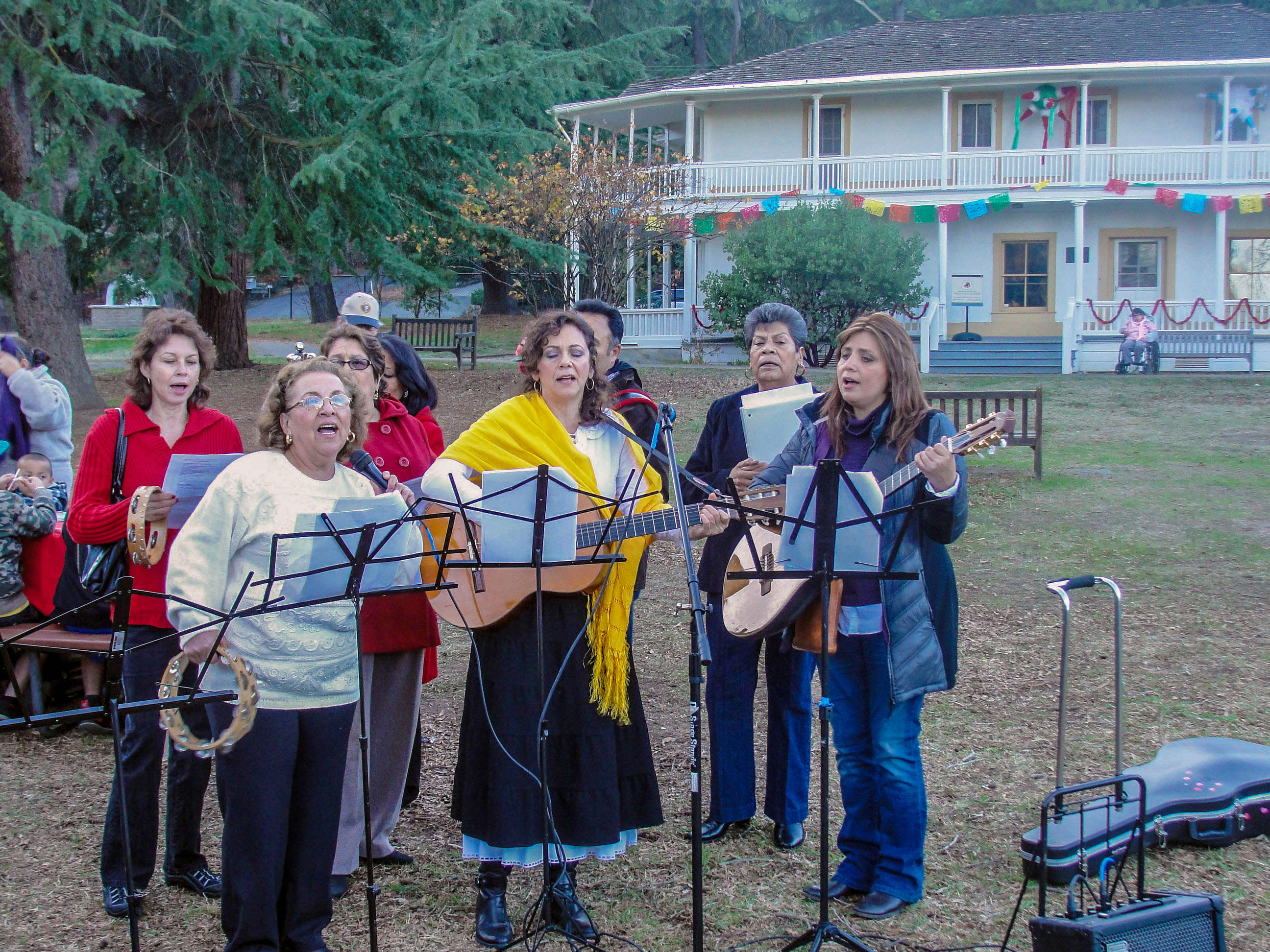 A festive choir sings and plays music outside a whitewashed decorated adobe.