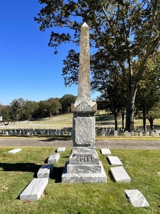 Obelisk grave marker surrounded by rectangular markers. "COLE" is seen inscribed.