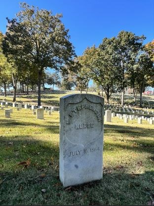 White headstone with the inscription, "E Stephenson. Nurse. July 16 1864." Trees and other headstones are in background.