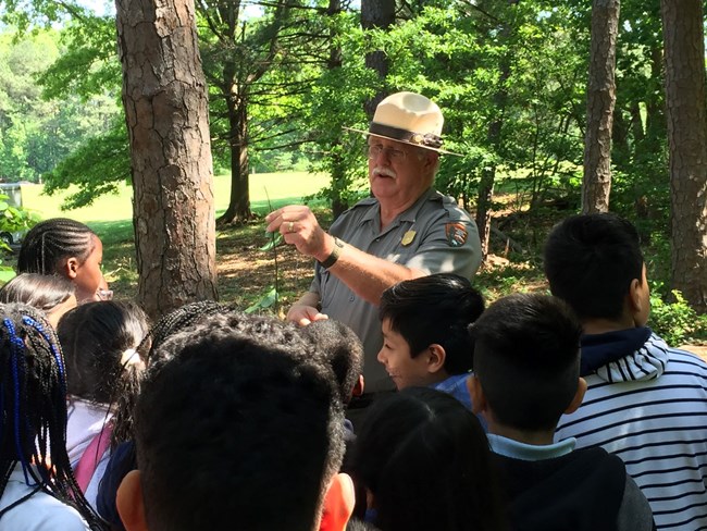 A park ranger shows students plant life out doors.