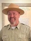 Man smiles wearing khaki park ranger uniform and hat.
