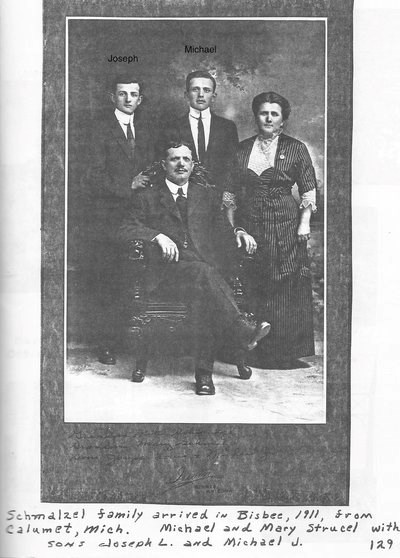 Three standing people and one sitting person pose for studio portrait.