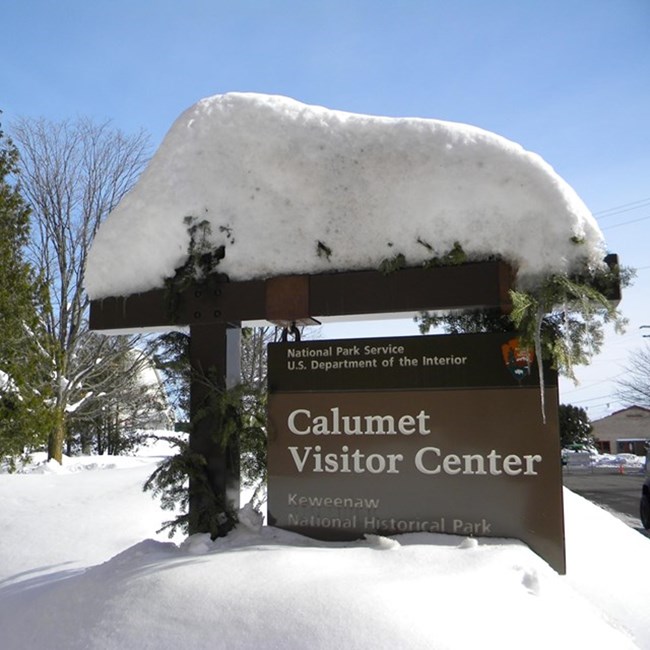 A sign covered in snow that reads Calumet Visitor Center.
