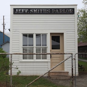 A white square building with large sign reading "Jeff. Smiths Parlor" stands behind a chain-link fence.