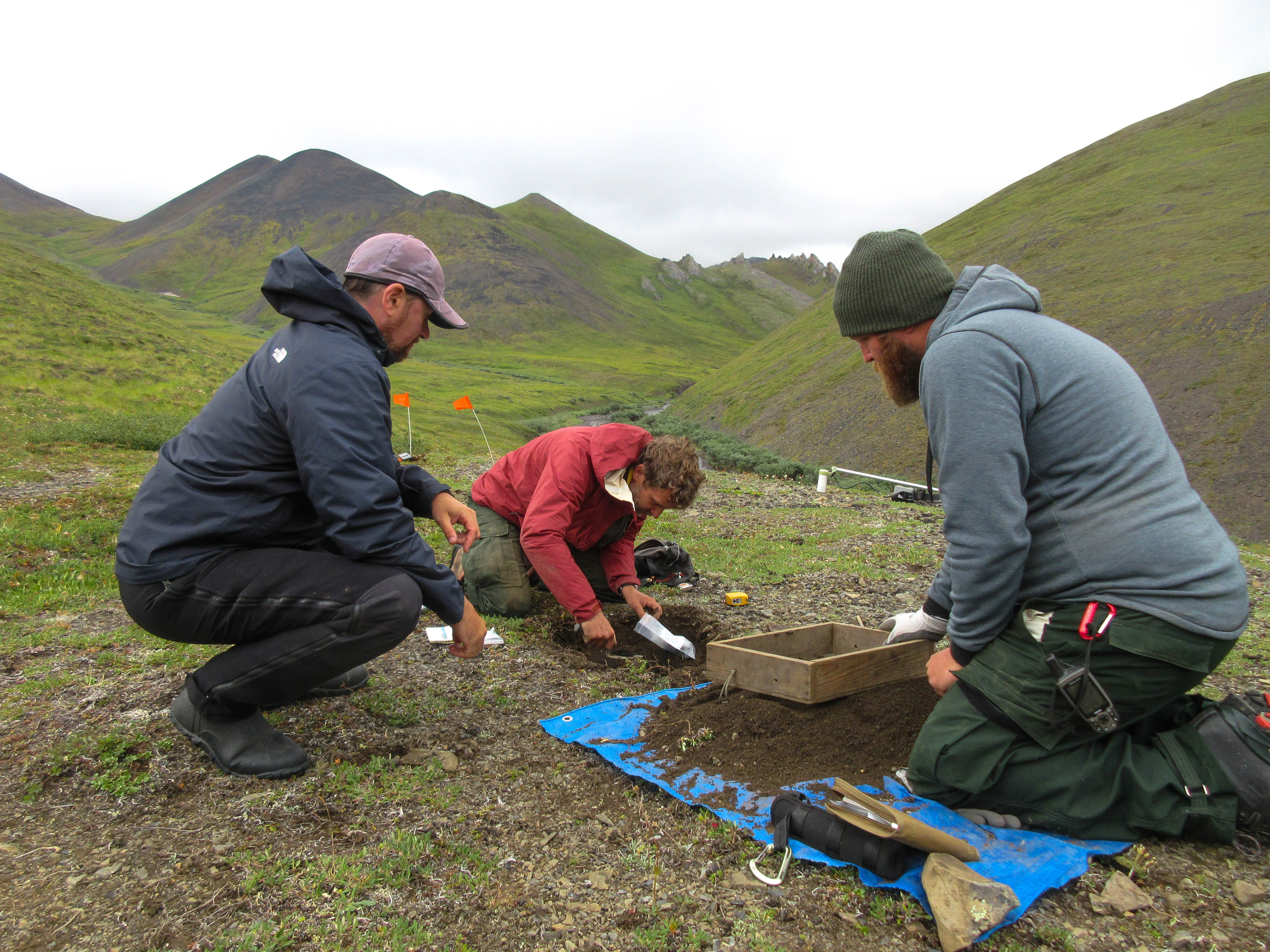 Three men use shovels to dig up soil to take samples of the soil