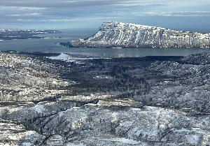 a lookout from a snowy mountaintop onto a coastal, mountainous island also covered in snow.