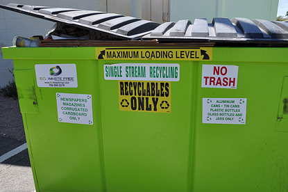 an closed green recycling dumpster surrounded by green garbage