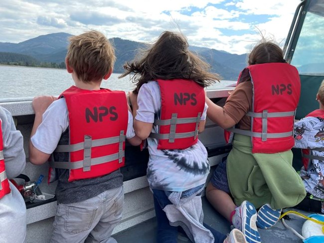 children wearing lifejackets sit in a boat looking out towards the water