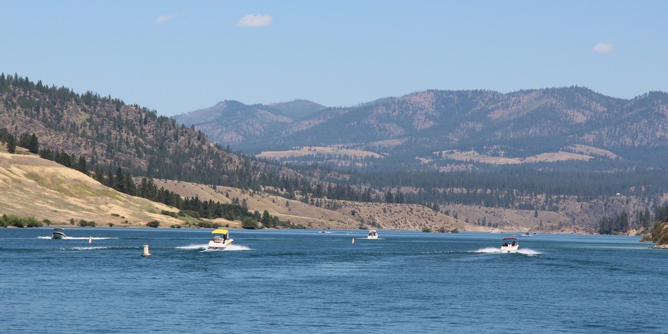 several motor boats out on the water on a sunner day, with low mountains in the background