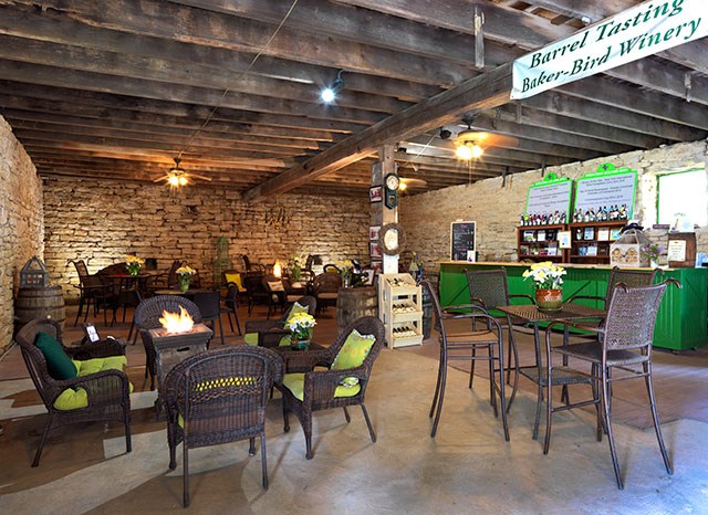 Baker Bird Winery-Lewis and Clark Travel A tasting room with tables and chairs is lined with a brick wall and wooden beams.