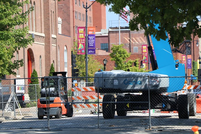 Large blue and orange construction vehicles sit on the street in front of red brick downtown buildings.