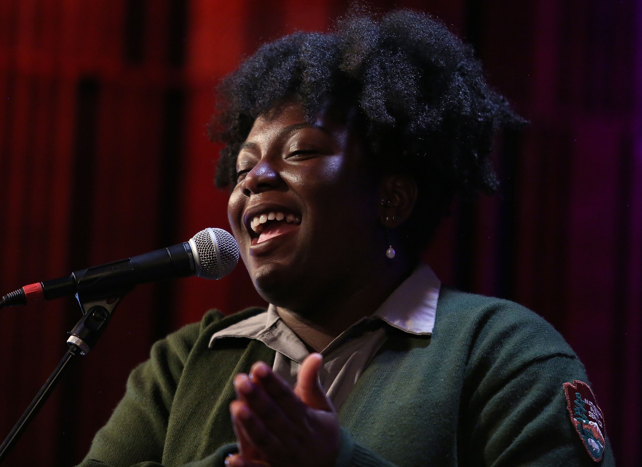 Jade Perdue, New Orleans Jazz National Historical Park A uniformed park ranger sings and claps in front of a dark red curtain background.