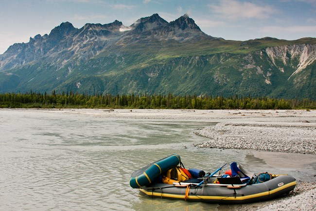 a raft rests on the shore of a river with mountains in the background