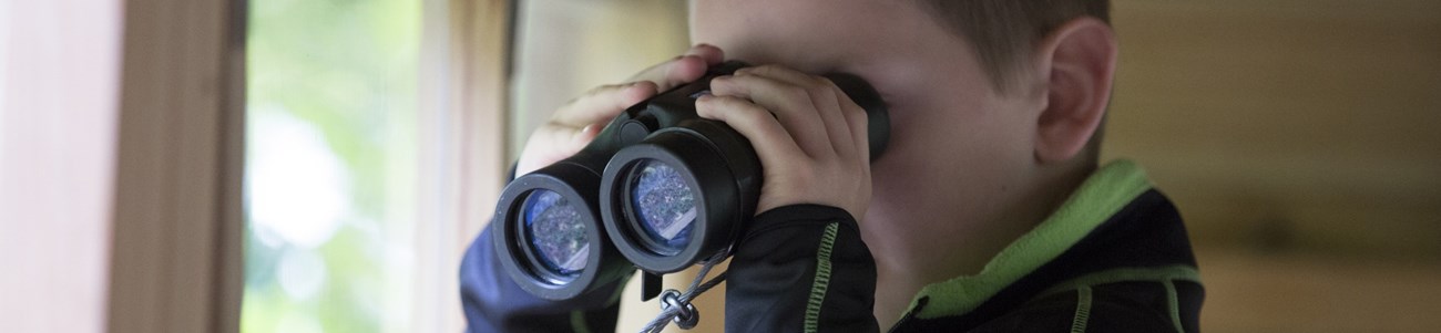 A small boy looks through binoculars.