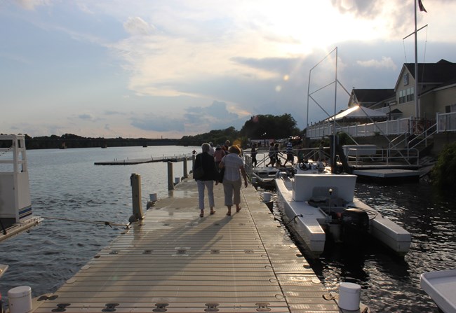 A group of people walk along a floating dock to return to land as he sun begins to set