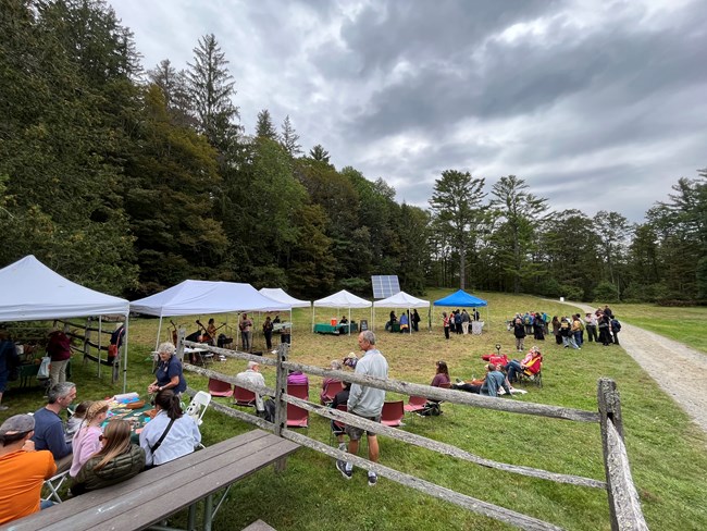 large pasture with 5 pop up tents and about 50 people standing about, band plays music under a tent