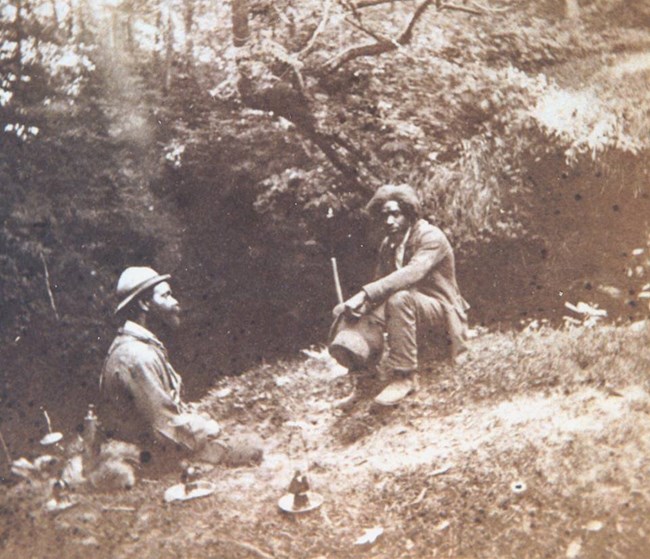 Two men sitting next to the entrance of the cave.