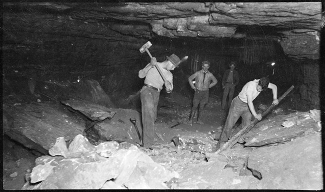 A black and white photos of men using hand tools to build a trail in the cave.