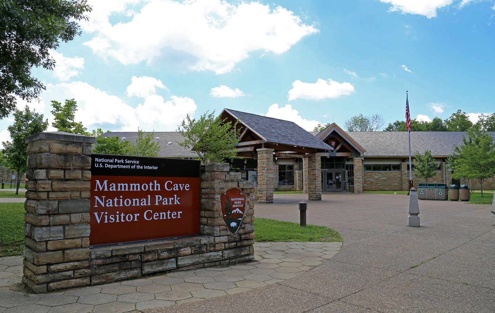 Image of large Mammoth Cave National Park Visitor Center sign with building and flagpole in the background.