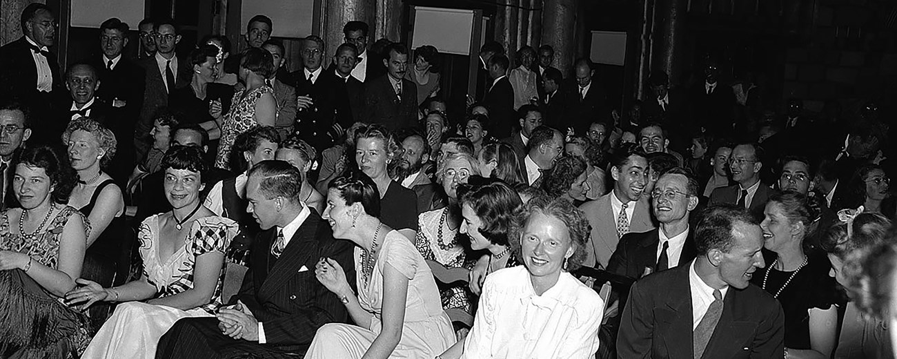 Many men and women seated in rows all facing the same direction wearing formal evening attire.