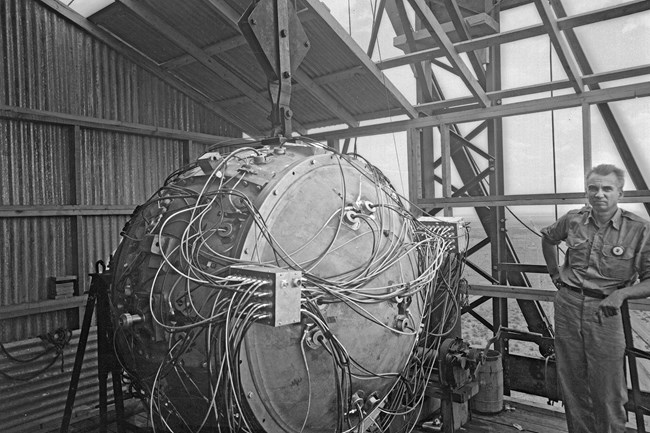 Black and white photo of man on left standing next to a ball with a lot of wires.
