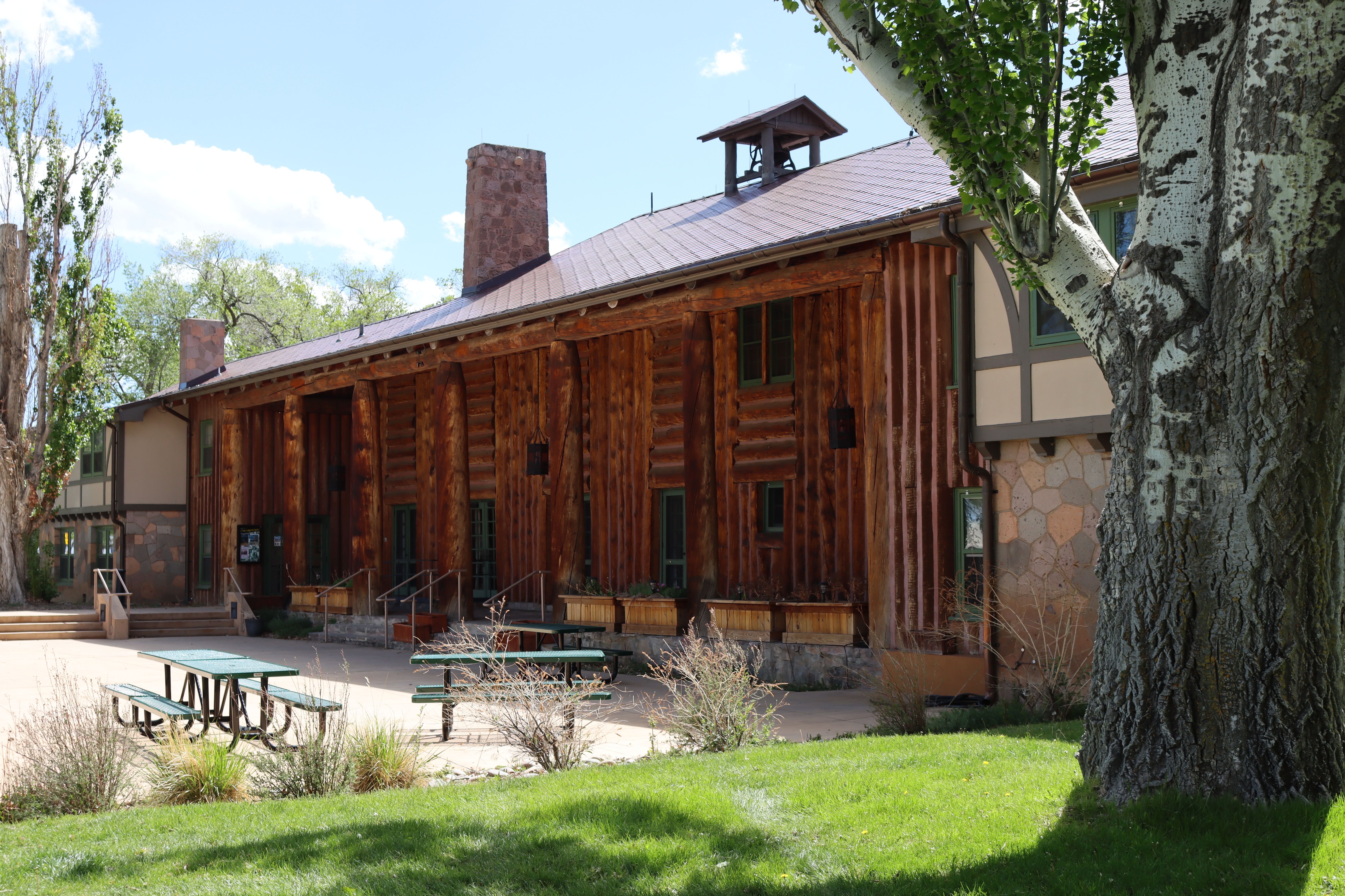 A three story wooden historic building with wood pillars framing porch, with grassy lawn in front.