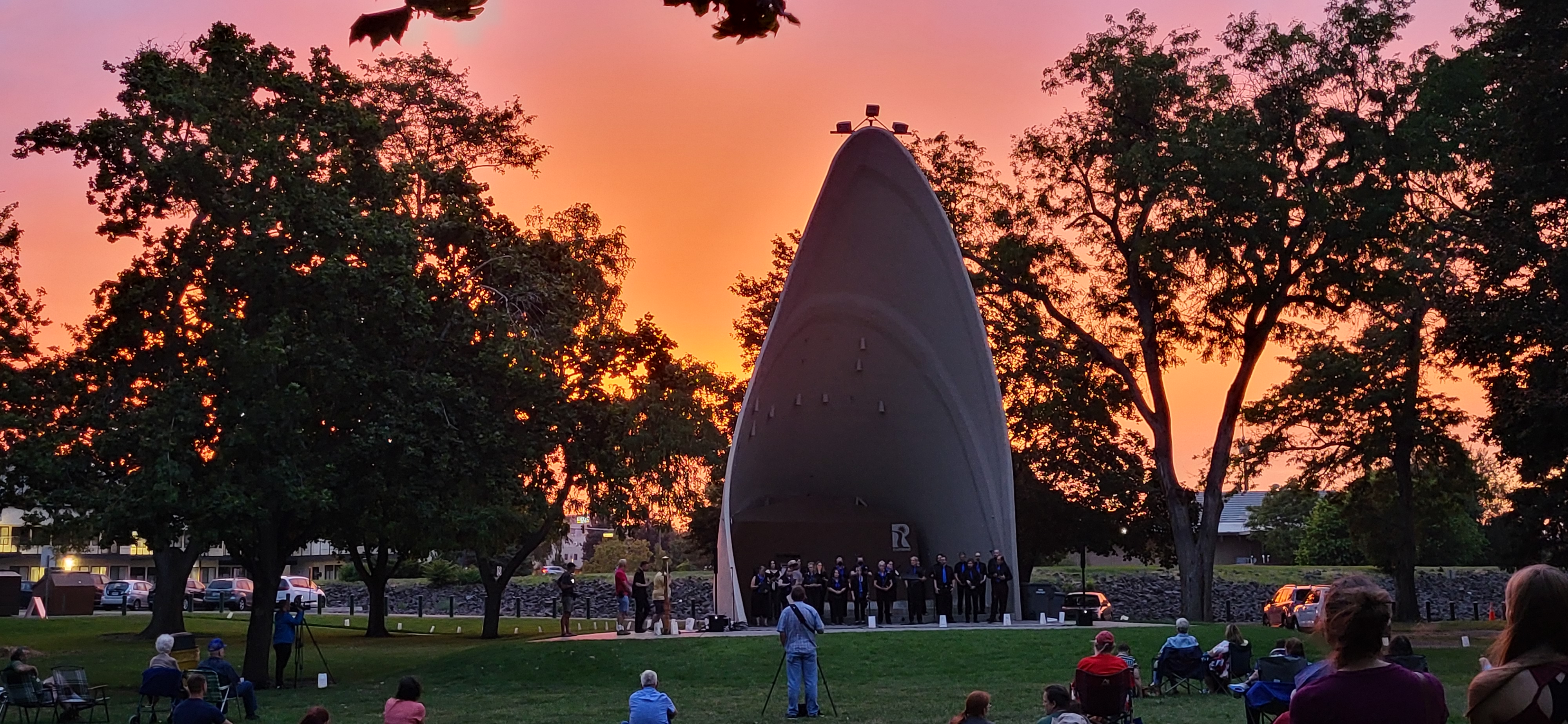 pink clouds brighten the sky behind a very tall and narrow 3-sided shelter with people gathered in front.