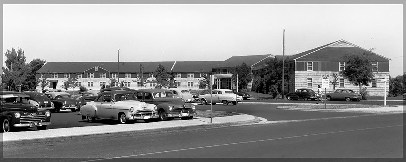 Black and white photo of classic cars parked in front of two story 1940s hotel.