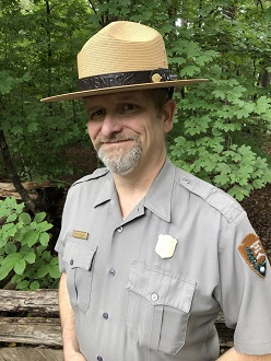 Park ranger in uniform standing in front of trees