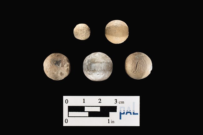 Five round lead musket balls of various sizes with a black background