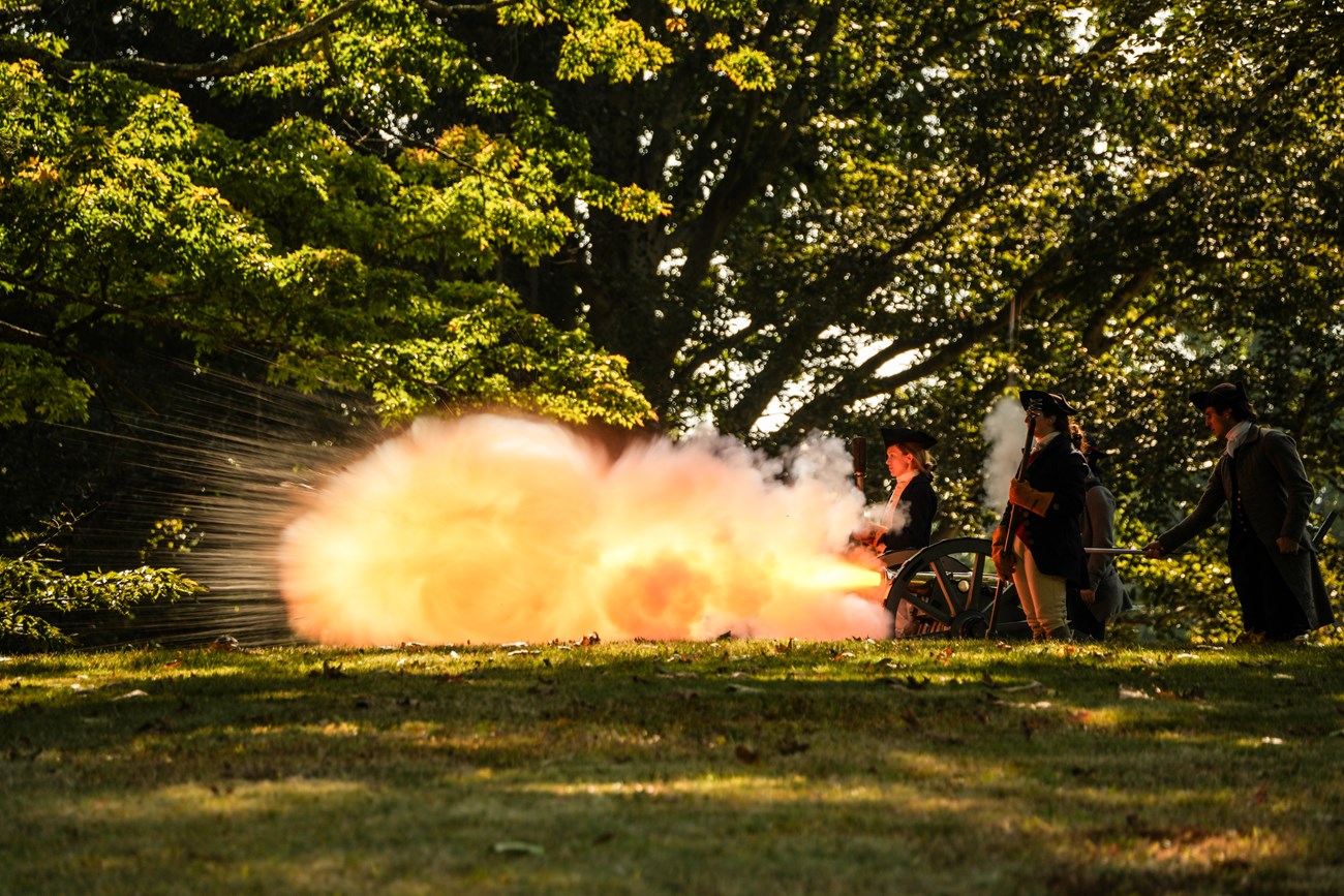 A small brass cannon firing with a large blast of flame coming from the front