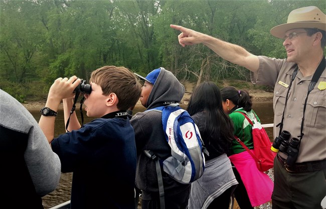 A park ranger points and students are looking through binoculars.