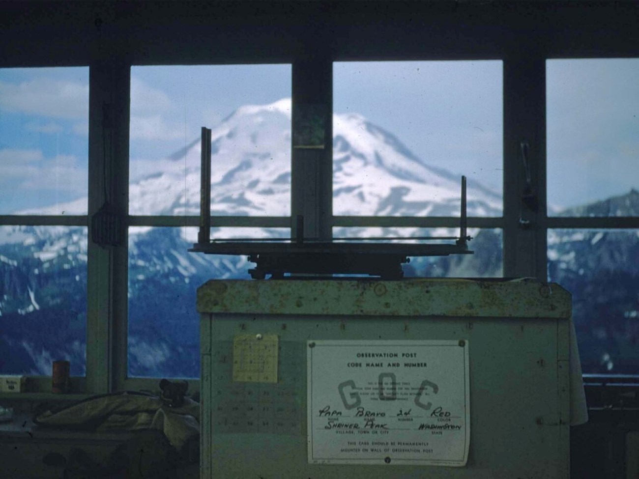 Historic photo of a vintage Osborn fire finder points towards Mount Rainier from the inside of a fire lookout.
