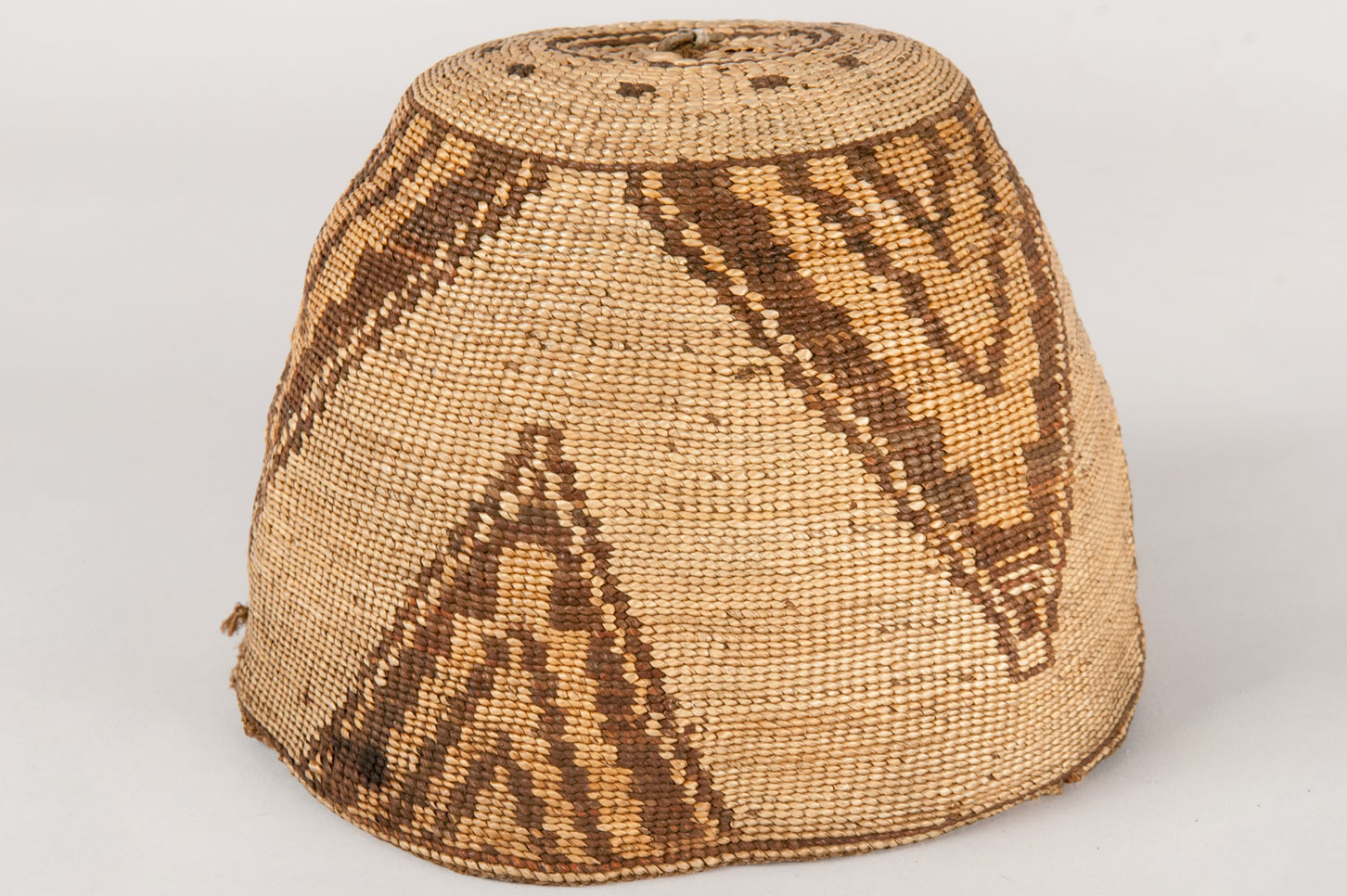 Subconical shaped basket hat made from hemp and beargrass. Designs on the outside of hat feature a three part division of separated dovetail and step patterns on a basal line of colors of orange and medium dark brown.