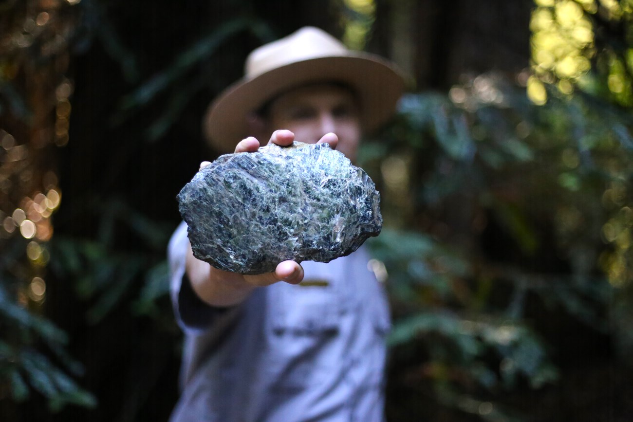 A blurry ranger holds a chunk of greenish-grey rock