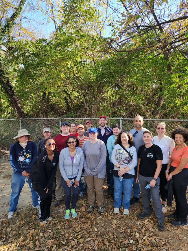 A group of people posing for a picture in front of a fence. Green vegetation can be seen behind the fence